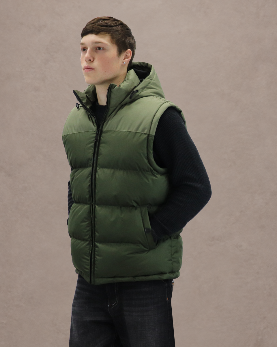Army Transit Hooded Vest, front-led three-quarter view on Trevor over a black knit against the lighter Warm taupe studio background